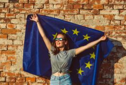 Młoda szczęśliwa kobieta trzymająca flagę Unii Europejskiej promującą koncepcję polityki UE
