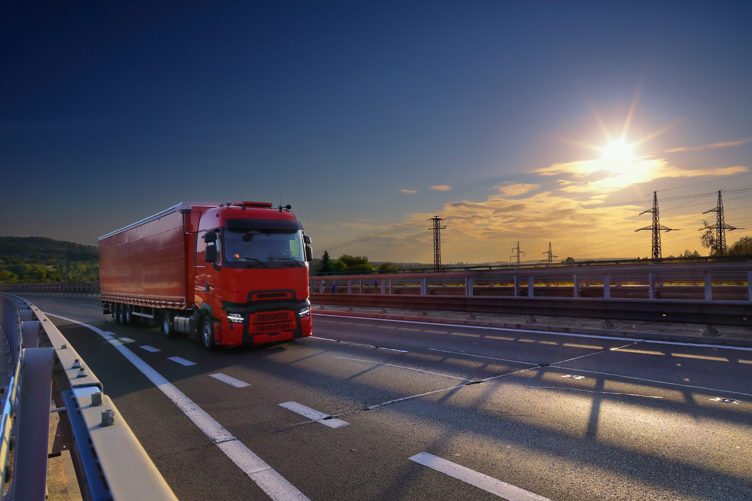 Czerwona ciężarówka jedzie autostradą przy zachodzącym słońcu