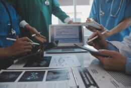 Doctors conduct consultations while standing around a table on which test results lie