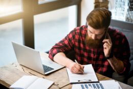 Bearded young man works on documents with open laptop next to