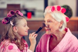 beautiful girl holding a cosmetic brush and applying powder to her grandmother's face